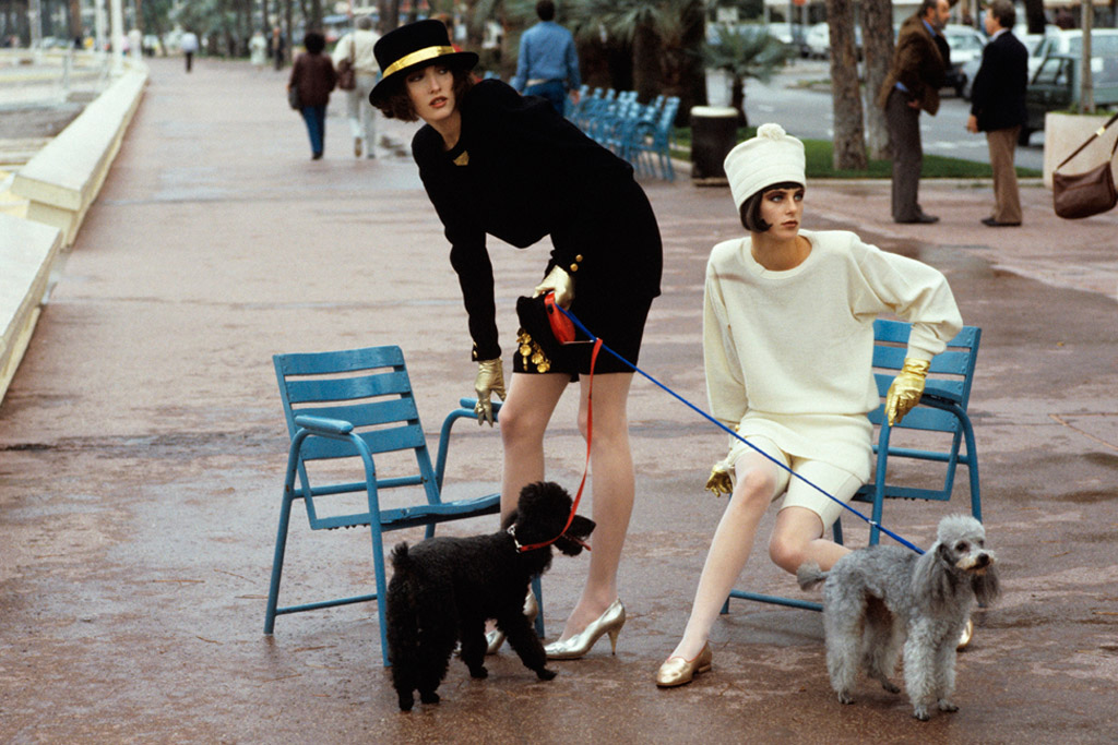 Models Tatjana and Laetitia Firmin-Didot holding two French poodles on leashes in a park; at left, both wear fashions by Sonia Rykiel. Circa January 1986.