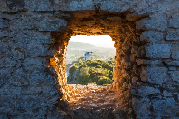 Старая мельница через окно в крепостной стене — стоковое фото