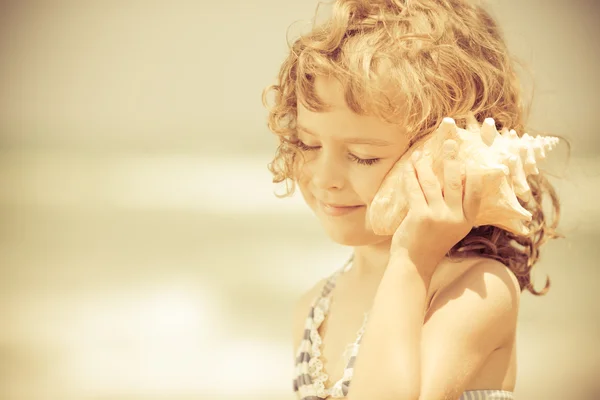 Счастливый ребенок слушать раковины на пляже — стоковое фото