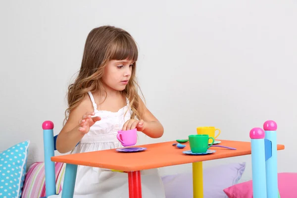 Маленькая девочка рисует сидя за столом в комнате на фоне серой стене — стоковое фото