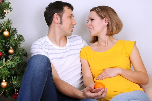 Молодая беременная женщина со своим мужем, сидя на полу возле елки в домашних условиях — стоковое фото