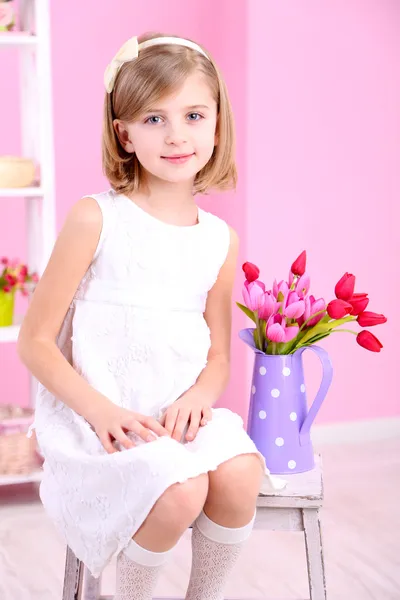Маленькая девочка сидит на небольшой лестнице с цветами на розовом фоне — стоковое фото