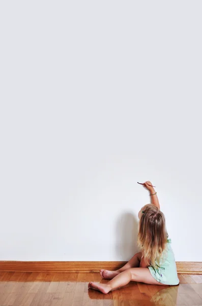 Девочка сидит на полу с помощью кисти и красок на стене — стоковое фото