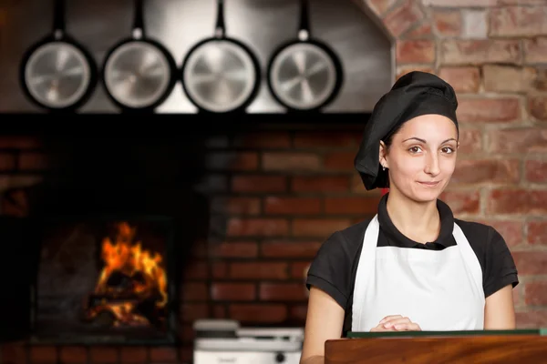 Стенд женщина шеф-повара на кухне вблизи дровяной печи — стоковое фото