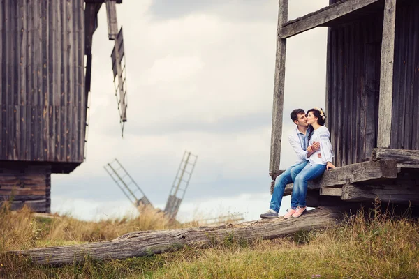 Молодая пара, целующаяся, сидя на шагах старой ветряной мельницы — стоковое фото