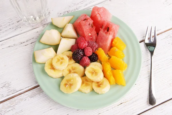 Нарезанные фрукты и ягоды на тарелку с стакан воды на деревянный стол — стоковое фото