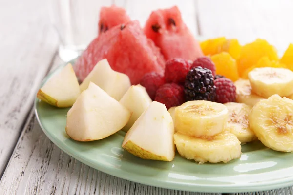 Нарезанные фрукты и ягоды на тарелку с стакан воды на деревянный стол — стоковое фото