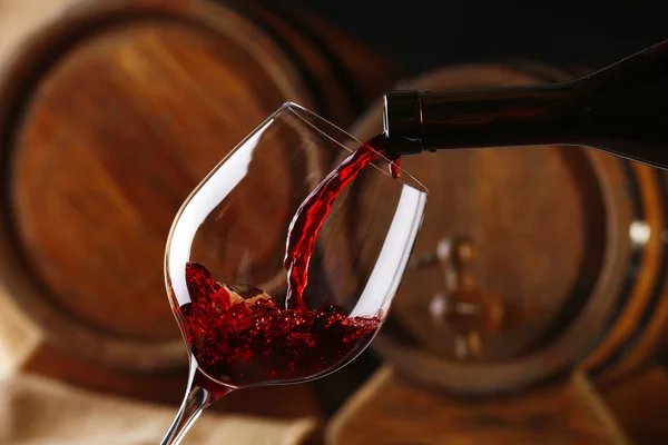 Заливка красного вина от бутылки в стекло с деревянными винными бочками на фоне — стоковое фото