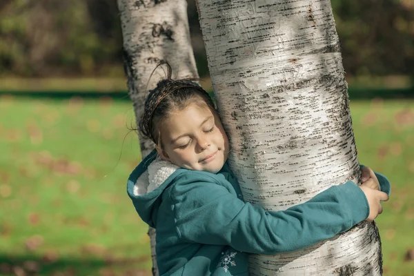 Радостная спокойная, красивая счастливая маленькая девочка закрытыми глазами, обнимая березы в осеннем парке и обладая ее досугом в солнечный теплый день — стоковое фото