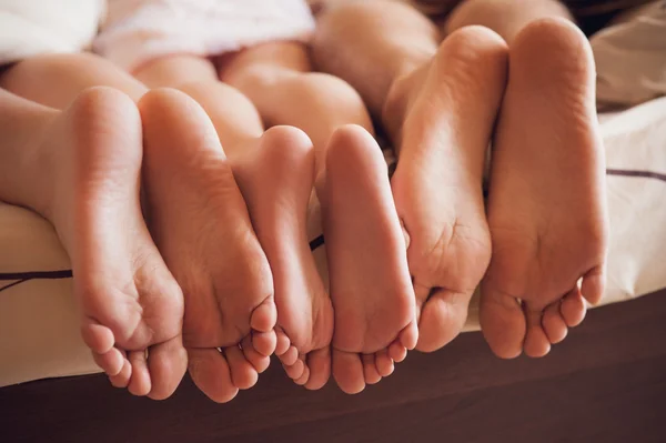 Заделывают семьи, демонстрируя свои ноги под одеялом — стоковое фото