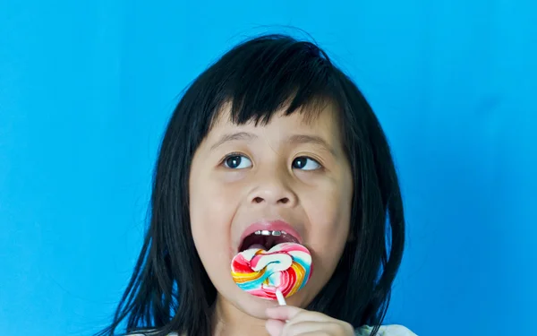 Портрет маленькая девочка лижет на сладкие конфеты. Изолированные на синий b — стоковое фото