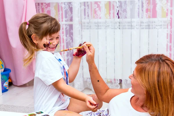 Мама рисует краски на футболку дочь, лежа на полу — стоковое фото