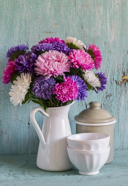 Цветы астры в белый эмалированный кувшин и vintage посуды - керамические чаши и эмалированные jar, на фоне синего деревянные — стоковое фото