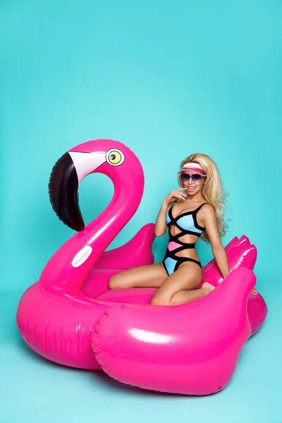 Потрясающие сексапильная блондинка модель в красочных бикини, лежит на розовый фламинго — стоковое фото