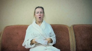 Медленное движение: молодая девушка в домашний халатик кашляет и чихает, сидя у себя дома на диване — стоковое видео