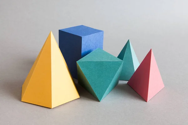 Красочные Платоновых тел, абстрактные геометрические фигуры на сером фоне. Пирамида Призмы прямоугольные куб желтый синий розовый зеленый цветные формы. Малая глубина резкости, копией пространства — стоковое фото