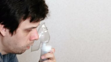 Используйте распылитель и ингалятор для лечения. Молодой человек, вдыхая через ингалятор маски и кашляет. Вид сбоку — стоковое видео