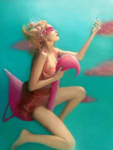 Портрет красивой блондинке с розовыми фламинго, летающие под водой в бассейне — стоковое фото