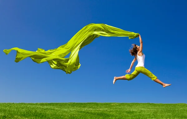 Женщина прыгает на зеленый луг с цветной ткани — стоковое фото
