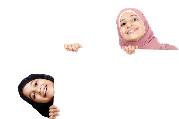 Две маленькие школьницы, проведение пустой белый знак для вашего сообщения. Хорошо для границ статьи или веб-сайтов. Красивые арабские мусульманские модели. Изолированные на белом фоне — стоковое фото