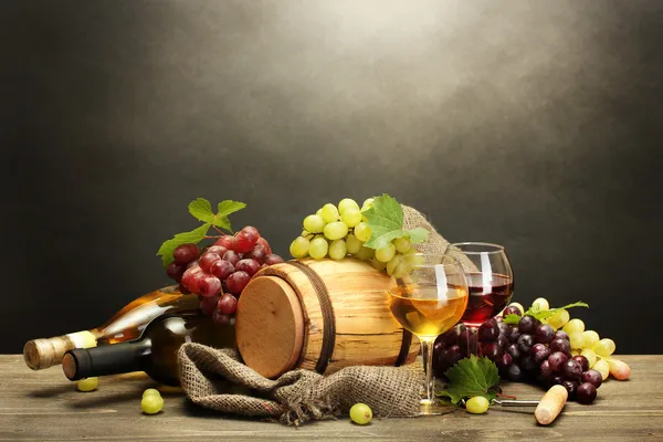 Ствол, бутылки и стаканы вина и спелый виноград на деревянный стол на сером фоне — стоковое фото