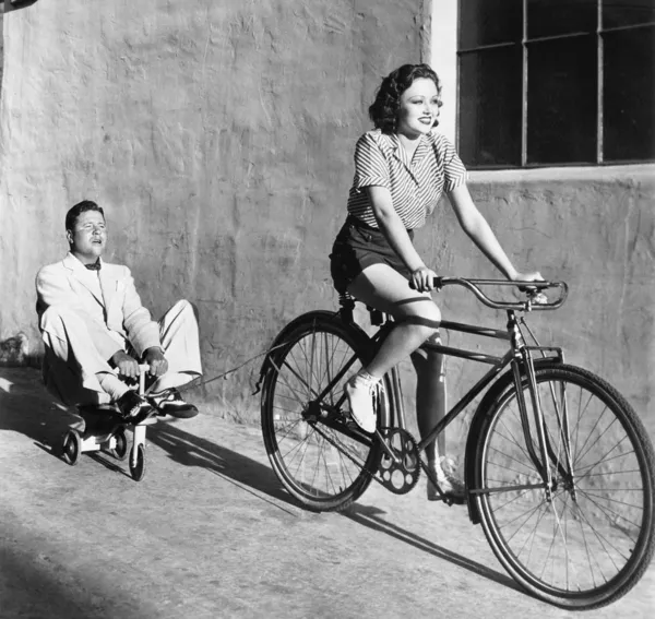 Женщина на велосипеде потянув взрослый человек на трехколесном велосипеде игрушка — стоковое фото