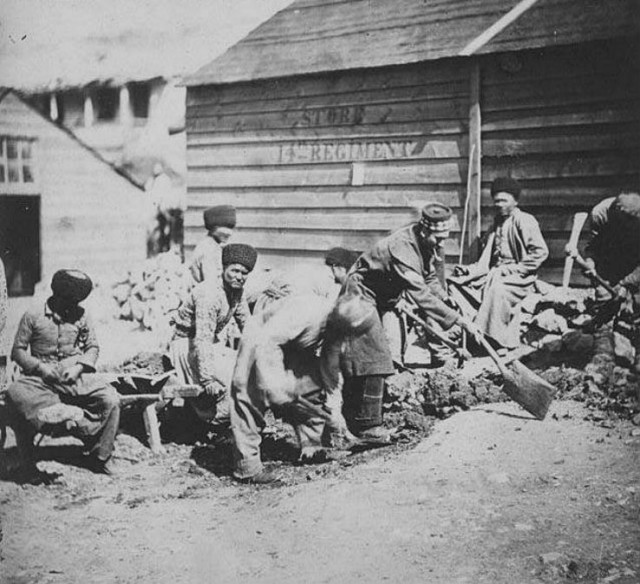 Группа крымских татар на работах по ремонту проезжей части в Балаклаве. На заднем плане деревянный сарай с надписью Store 14 th Regiment( склад 14-го полка). 1855 год..jpg