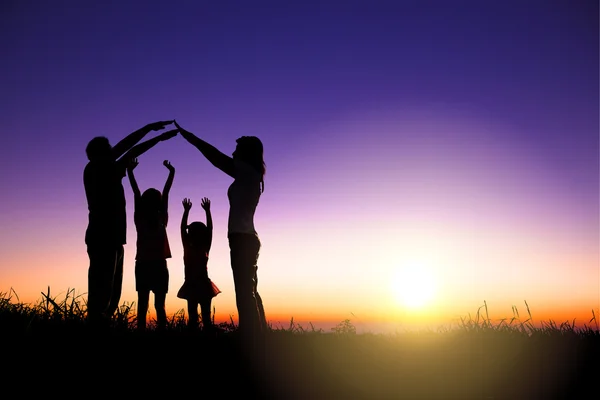 Счастливая семья, делая дома знак на холме с восхода солнца backgroun — стоковое фото