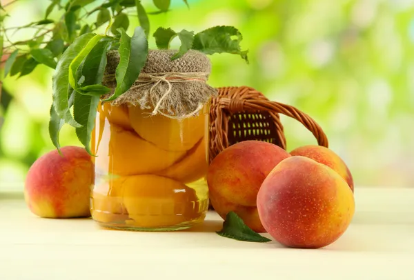 Банку консервированных персиков и свежие персики на деревянный стол, за пределами — стоковое фото