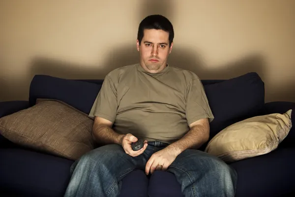 Скучно, overweight человек сидит на диване — стоковое фото