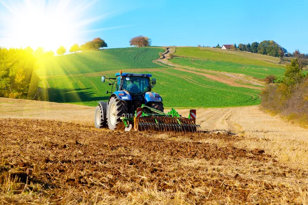 Трактор пашет поле весной, с солнечным светом — стоковое фото