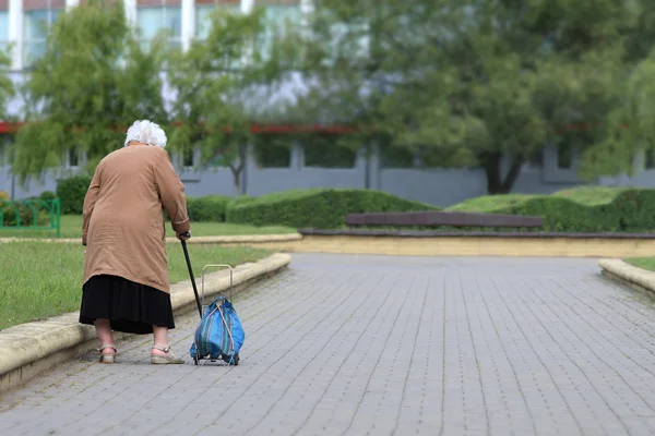 Старость - не радость. Старая женщина с мешком сзади. Старая женщина устала — стоковое фото