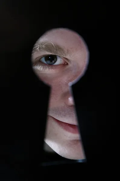 Человек глаз смотрит через отверстие в замочную скважину, на черном фоне — стоковое фото