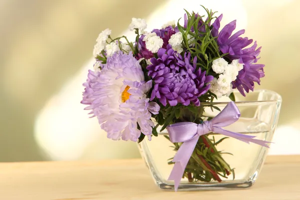 Красивый букет ярких цветов в стеклянной вазе, на деревянном столе, на светлом фоне — стоковое фото