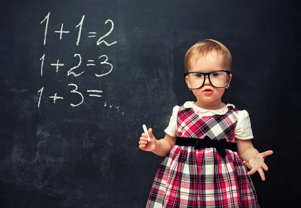 Девочка в очках и мелом на школьной доске с arithmeti — стоковое фото