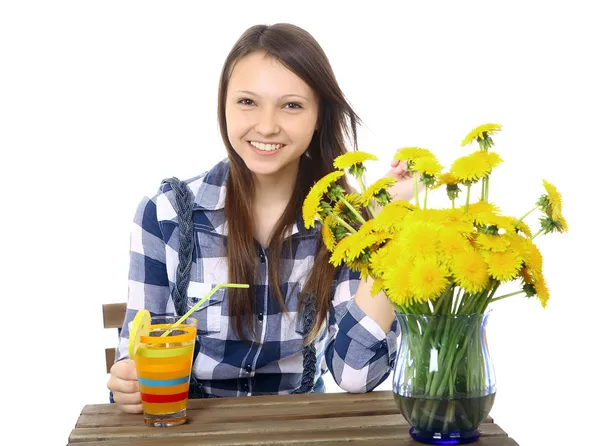 Девушка подросток, Кавказский вид, брюнетка, в клетчатой рубашке, держа стакан напитка. на столе находится Голубая ваза, с букетом желтых цветов, одуванчики. одна девушка, Кавказская — стоковое фото