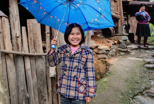 Сельских Азиатская девушка, около 8 лет, скрывая синий зонтик и смеяться Лицензионные Стоковые Изображения