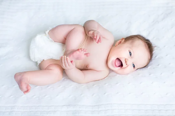 Смех ребенка носить подгузник, играя с ее ноги — стоковое фото