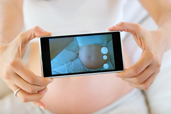 Беременная женщина берет фотографию ее живот — стоковое фото