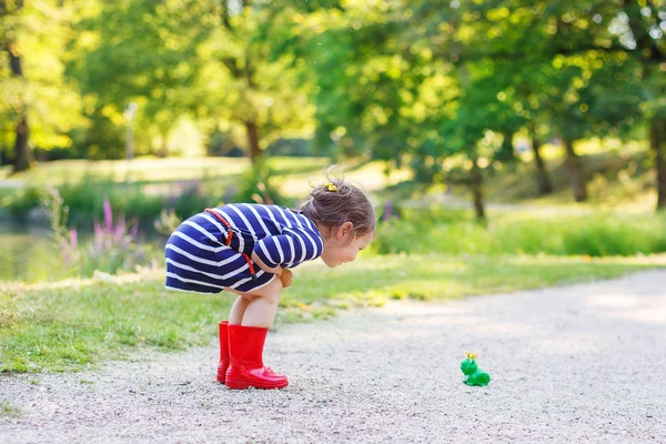 Красивая девочка в красного дождя сапоги, играя с резиновые лягушки — стоковое фото