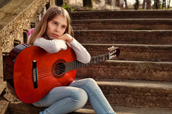 Мечтательная девушка Холдинг на гитаре в коленях против старой каменной лестницы — стоковое фото