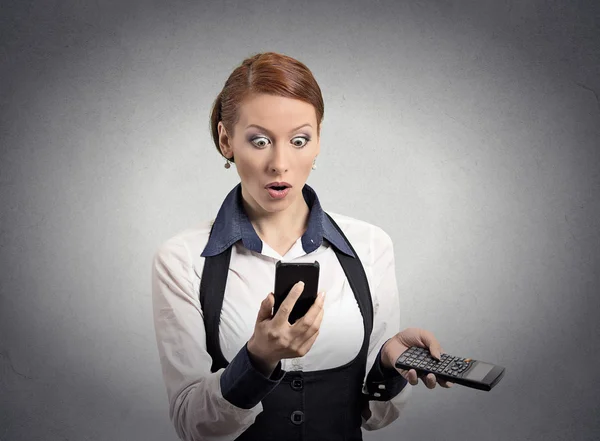 Потрясенная женщина, считающая смартфон, держащий калькулятор — стоковое фото