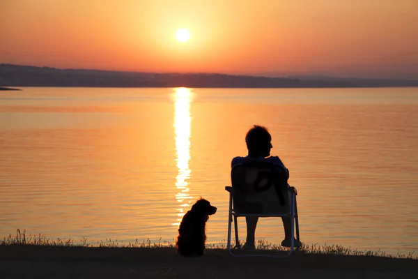 Человек и его собака друг на море можно любоваться восходом солнца — стоковое фото