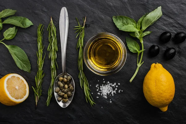 Травы смешать с лимонами, каперсов и оливок на черном каменном столе — стоковое фото