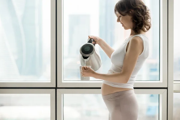 Беременная женщина, делая чашку горячего напитка — стоковое фото