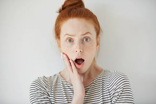 Young redhead woman with surprised facial expression looking at the camera, screaming with mouth wide open. Female shocked with sale prices while shopping online. Human face expressions and emotions — стоковое фото