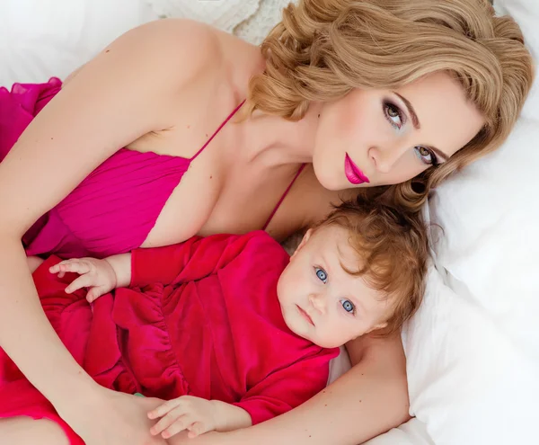 Красивый тонкий блондинка мама в красном платье лежит на кровати рядом с s — стоковое фото