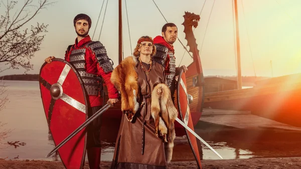 Славянские Принцесса и два воина с мечами и щитами на фоне военных кораблей — стоковое фото