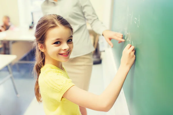 Маленькая улыбчивая школьница, пишущая на классной доске Лицензионные Стоковые Изображения
