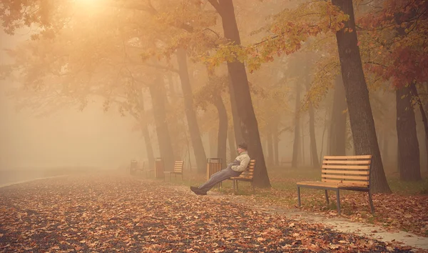 Человек сидеть на скамейке в парке в туманный день — стоковое фото